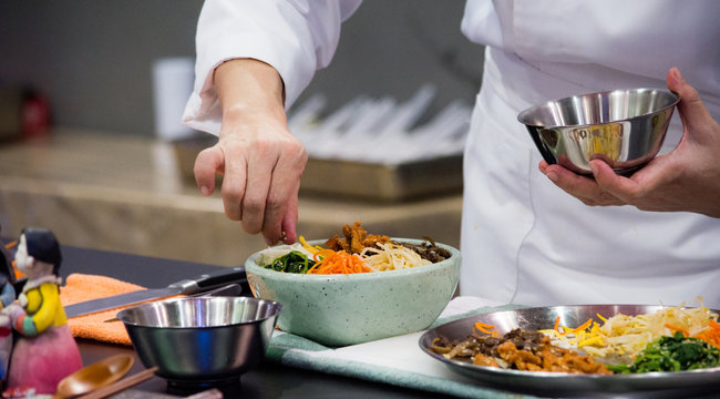 Korean restaurant kitchen with chef preparing bibimbap and banchan