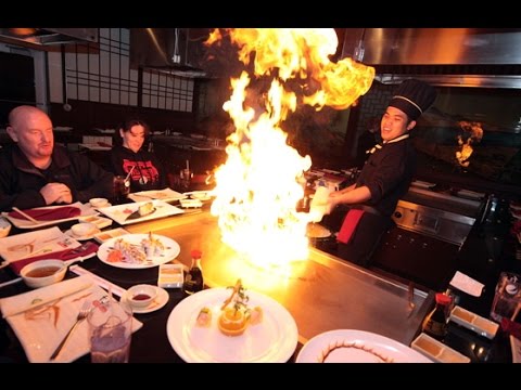 Hibachi chef cooking on teppanyaki grill with flaming dish for guests